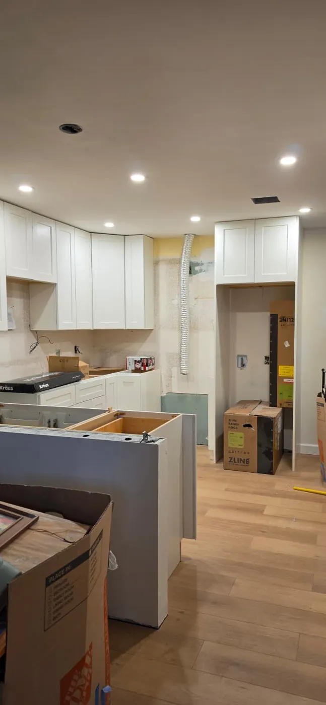 Kitchen mid-build with white shaker cabinets installed, recessed lighting, and new plank flooring